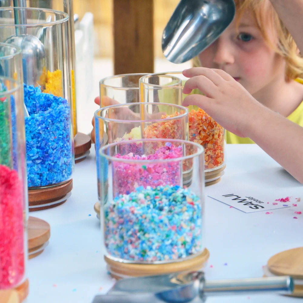 Enfant manipulant des copeaux de plastique colorés lors d’un atelier Samji.