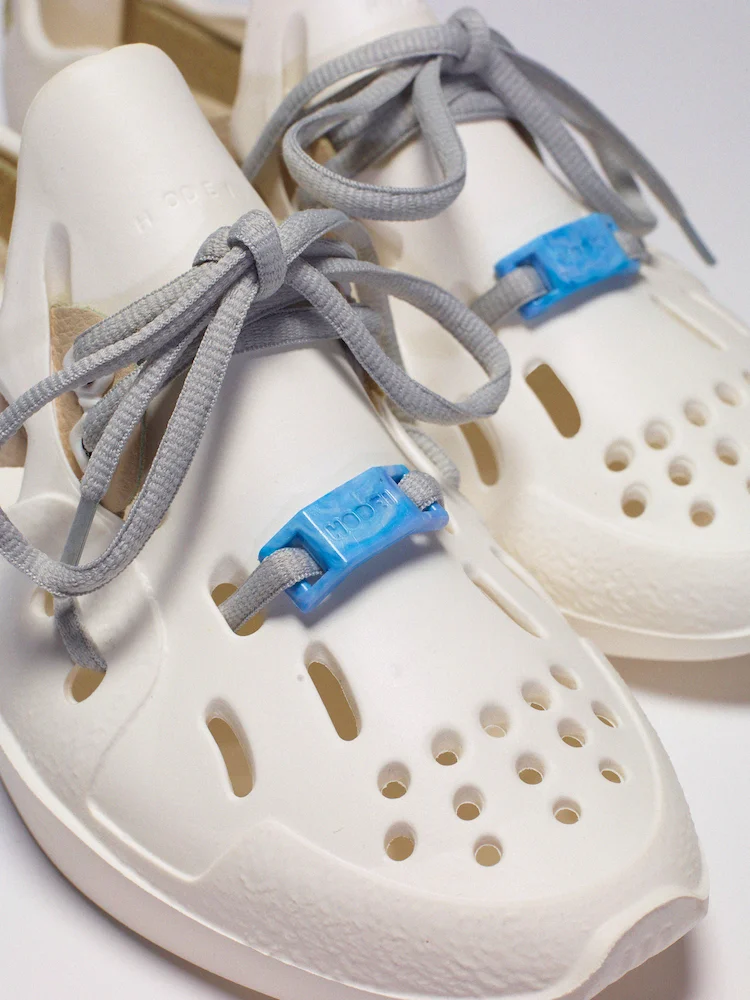 Gros plan sur chaussures Hodei blanches avec lacets gris et accessoires bleus recyclés.